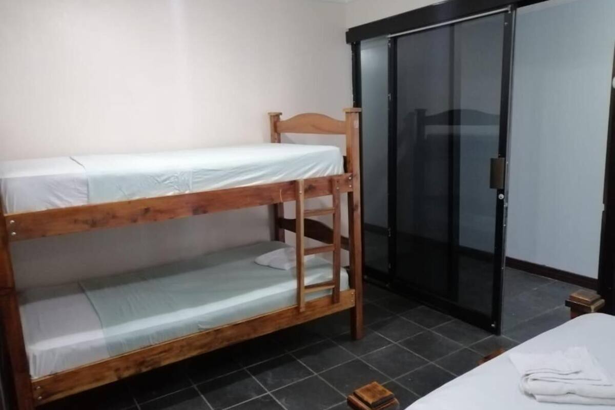 Una cama litera en una habitación con armario de puertas correderas y un pequeño taburete de madera.