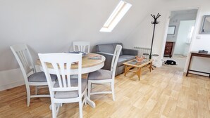 Una sala de estar moderna con una mesa de comedor redonda, sillas blancas, un sofá gris y una mesa de centro de madera.