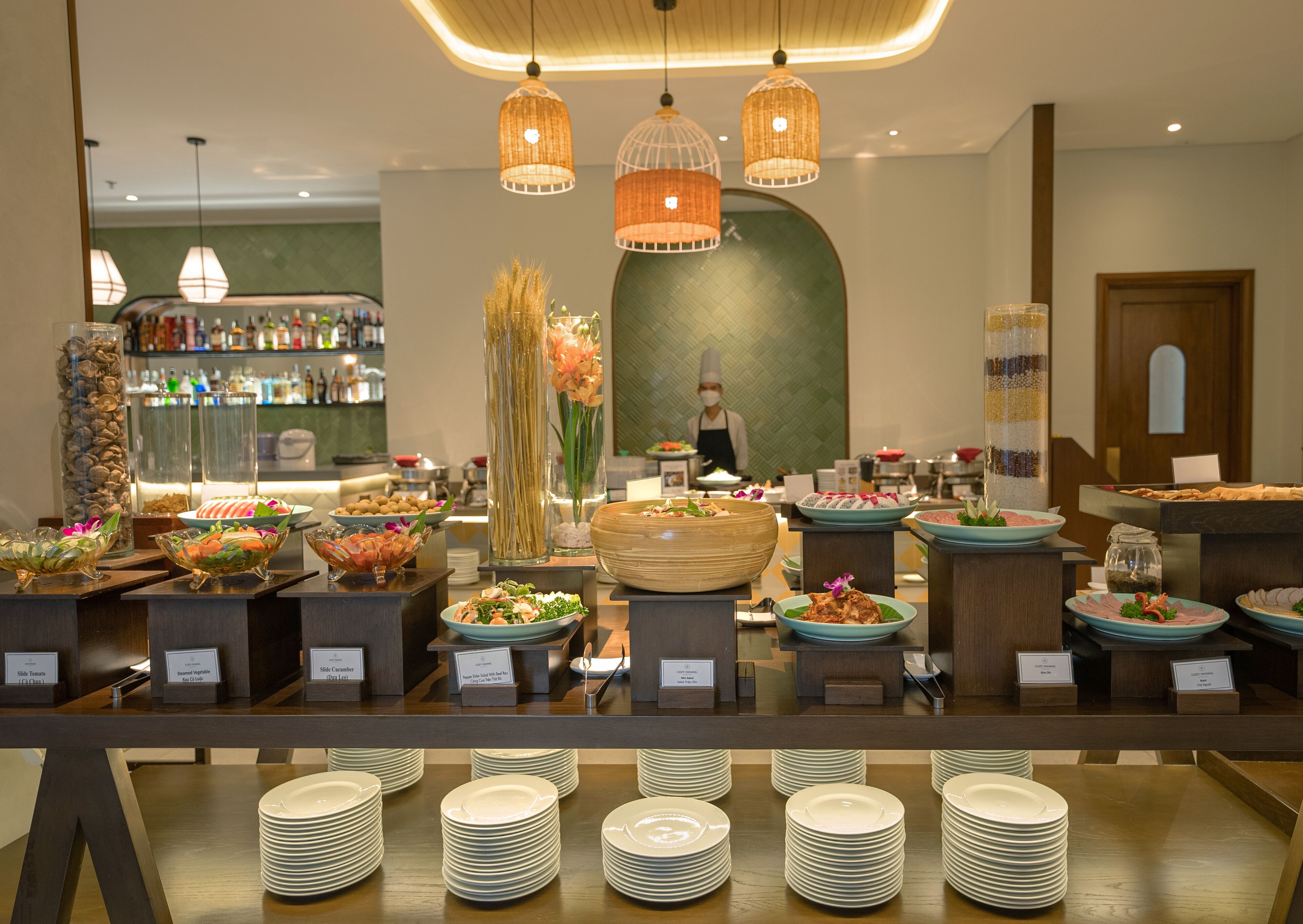 A buffet setup with various food stations, including salads, seafood, and desserts, in a well-lit room with hanging pendant lights.