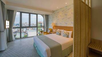A hotel room with a large bed, a view of the city, and a decorative partition.