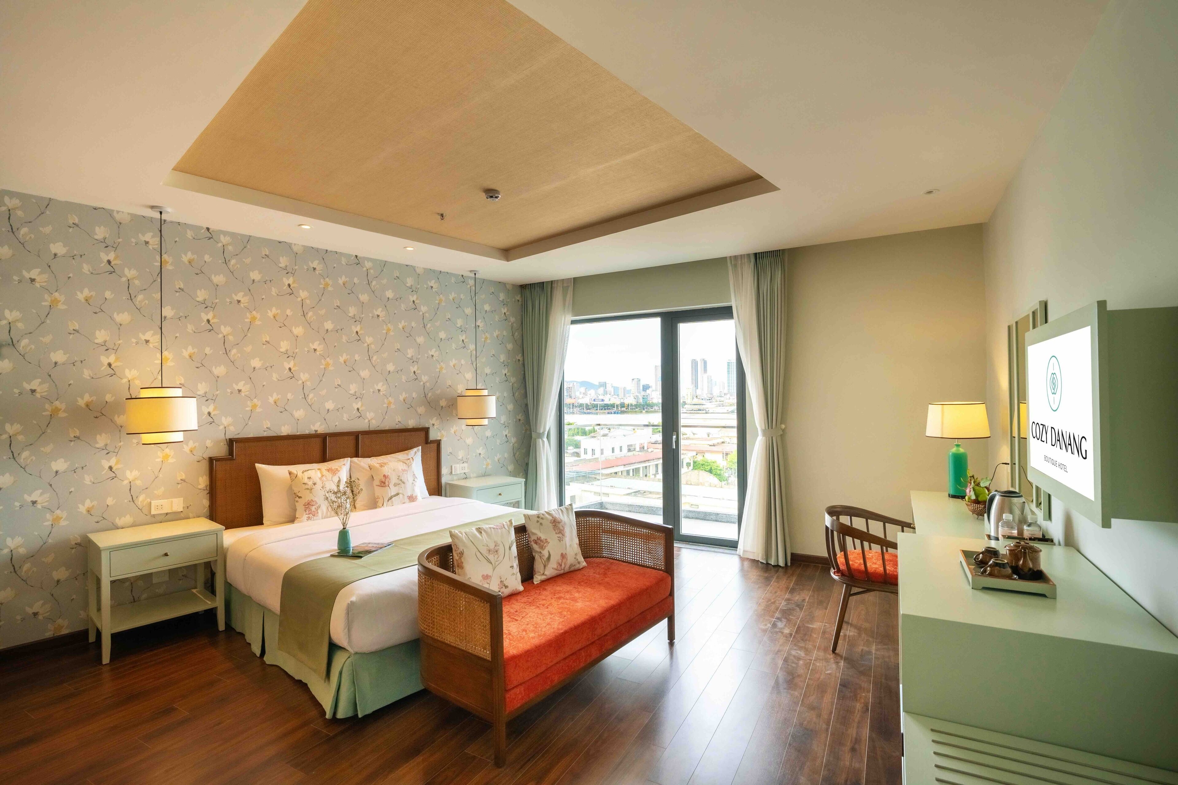 A hotel room with a bed, a sofa, a desk, and a large window with a city view.