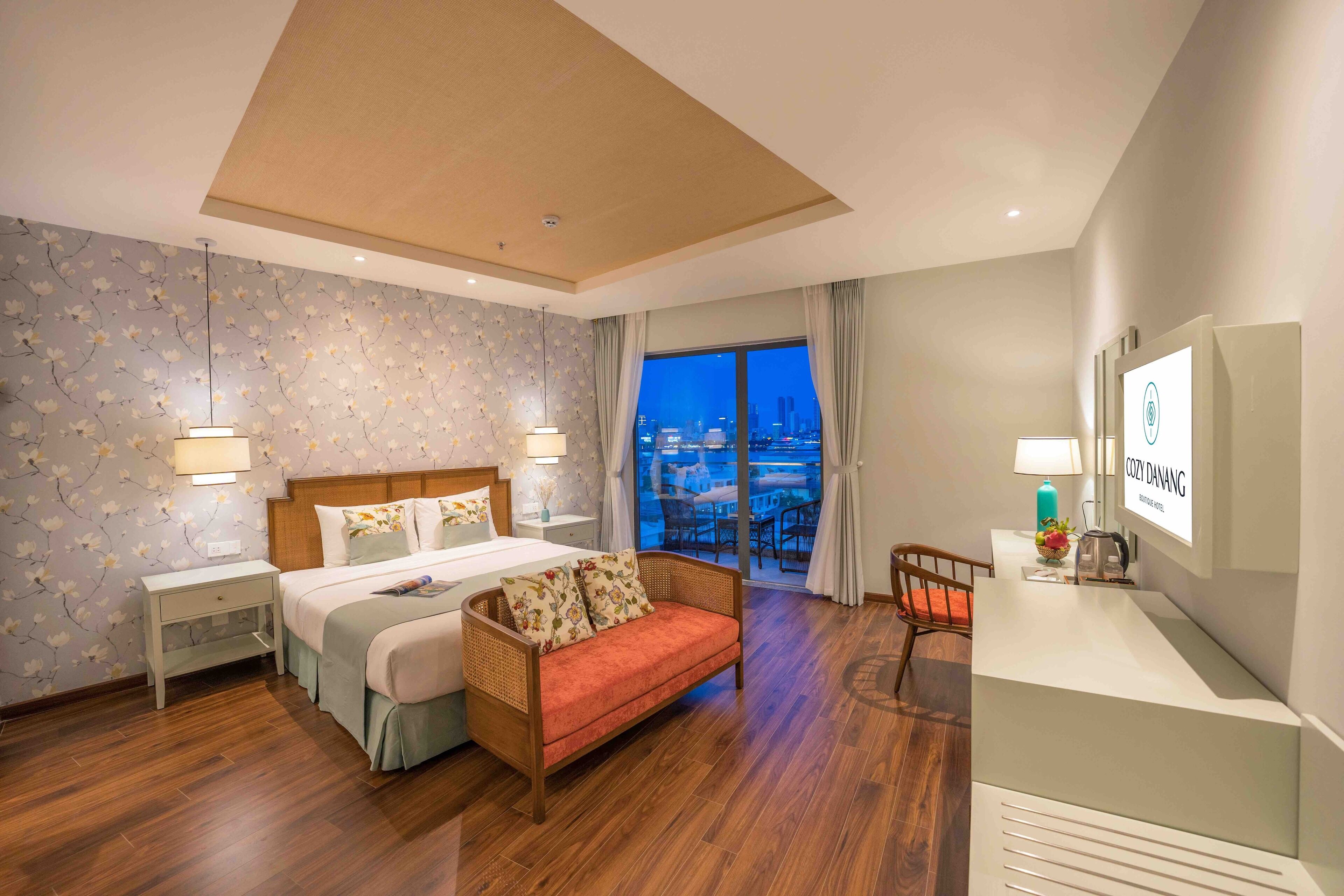 A hotel room with a bed, a sofa, a desk, and a view of the city at night.