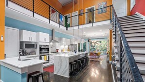 Una cocina moderna con una isla central, taburetes de bar y una escalera que sube a un nivel superior.