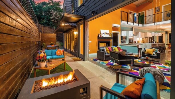 Un espacio exterior moderno con un hogar, sofás y una cocina visible a través de una puerta abierta.