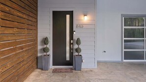 Una entrada de casa moderna con una puerta oscura, un buzón y dos macetas.