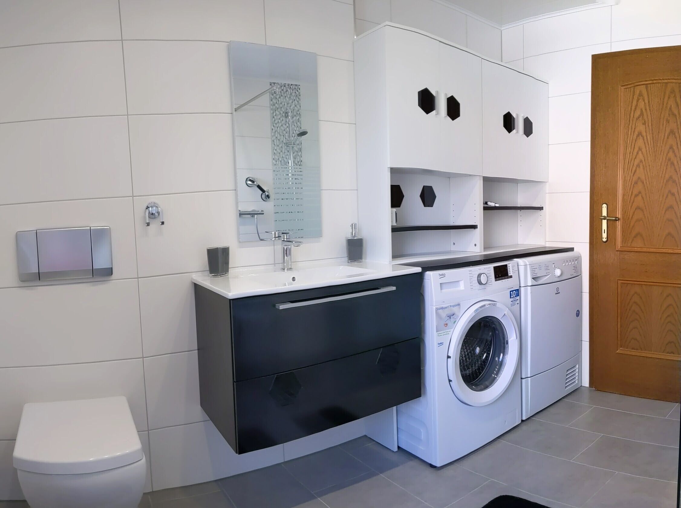 Ein modernes Badezimmer mit Toilette, Waschbecken, Spiegel, Dusche und Waschmaschine.