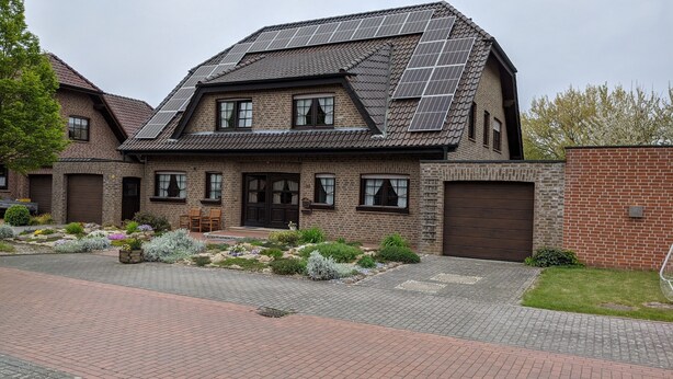 Ein zweistöckiges Haus mit Schrägdach, Solaranlage und Ziegelverkleidung.