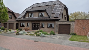 Une maison à deux étages, dotée d’un toit en pente, de panneaux solaires et d’une façade en briques.