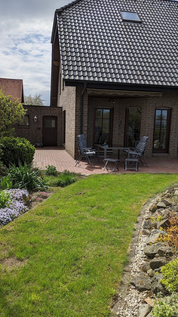 Une maison en briques avec un toit en tuiles, une terrasse avec des meubles d’extérieur et un jardin bien entretenu.