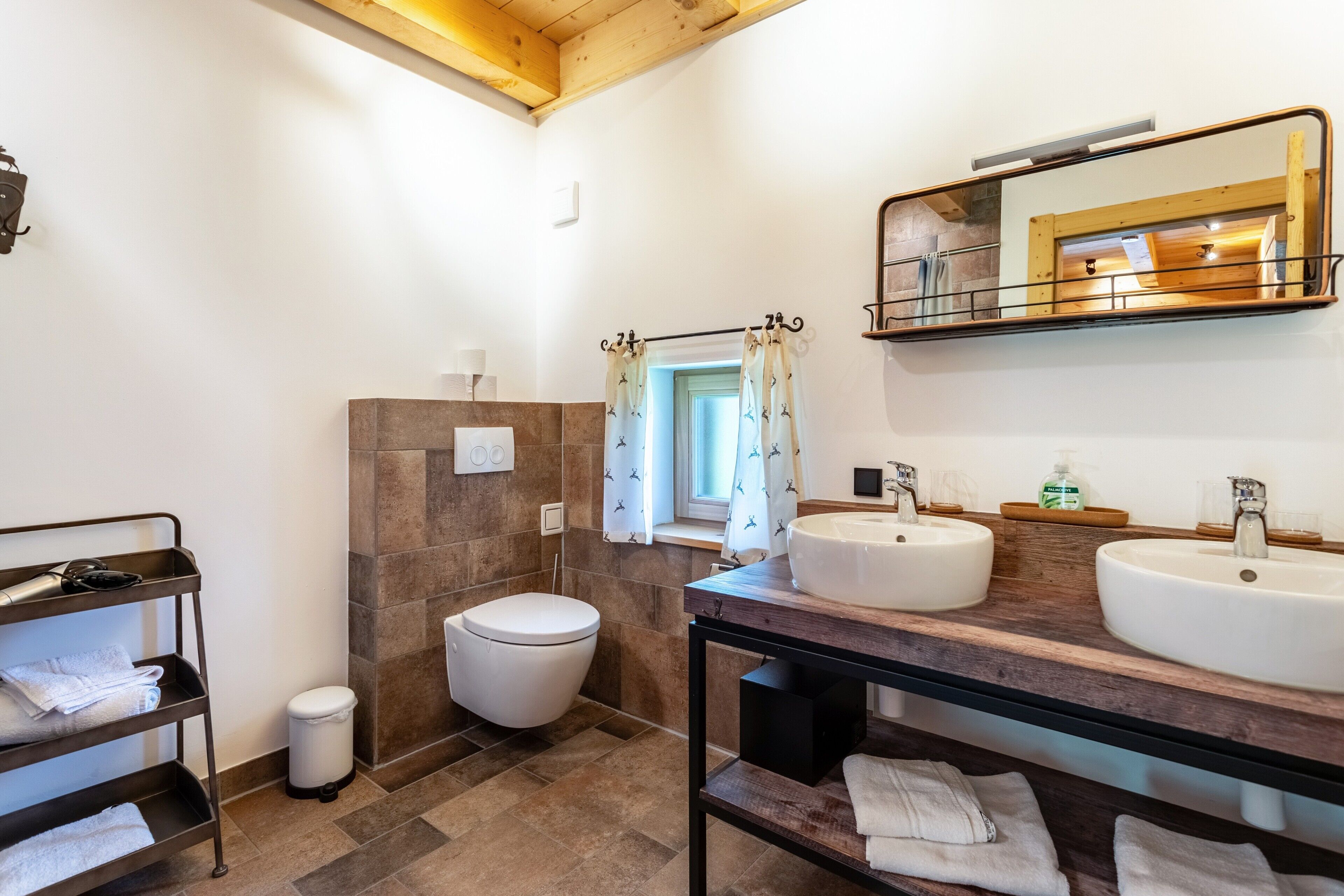 A bathroom with two sinks, a toilet, a shower with curtains, a towel rack, and a mirror.