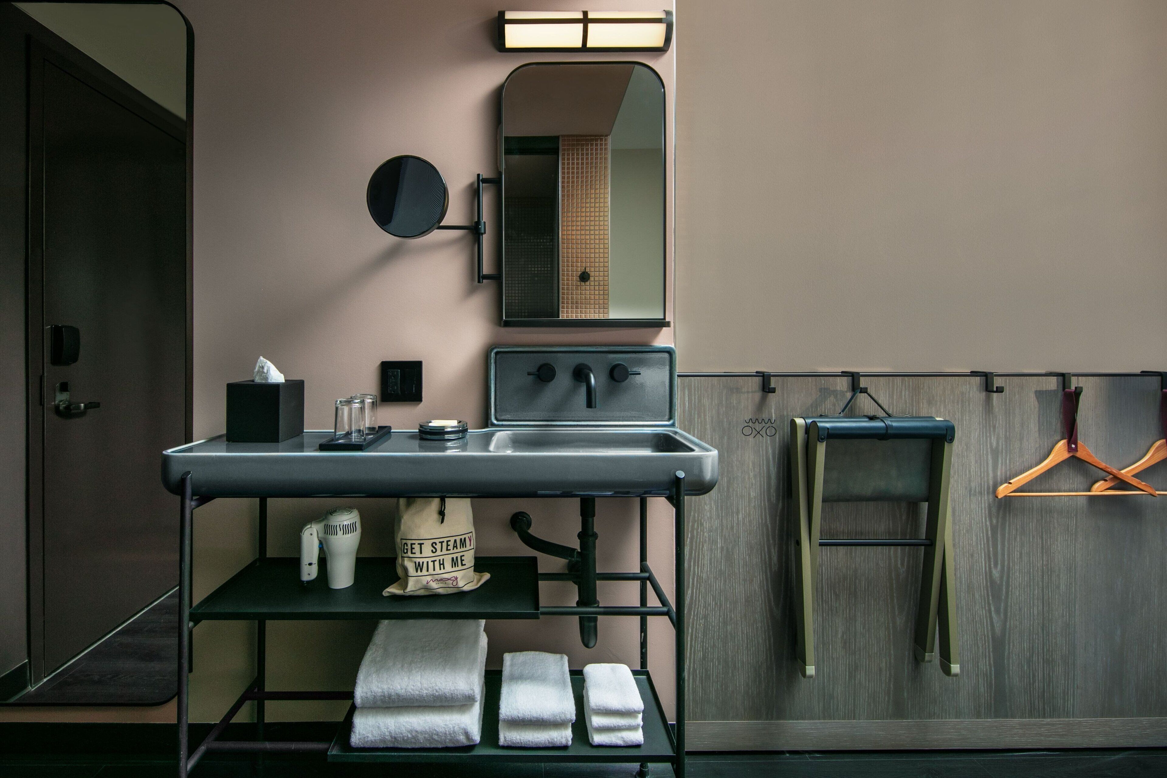 A modern bathroom with a sink, mirror, towel rack, and a hanging garment.