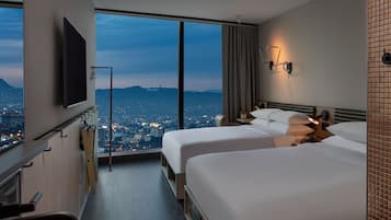 A hotel room with two beds, a TV, a city view, and a sliding door to the balcony.