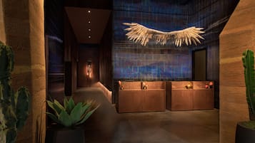 A modern reception area with a large winged light fixture, a reception desk, and potted plants.