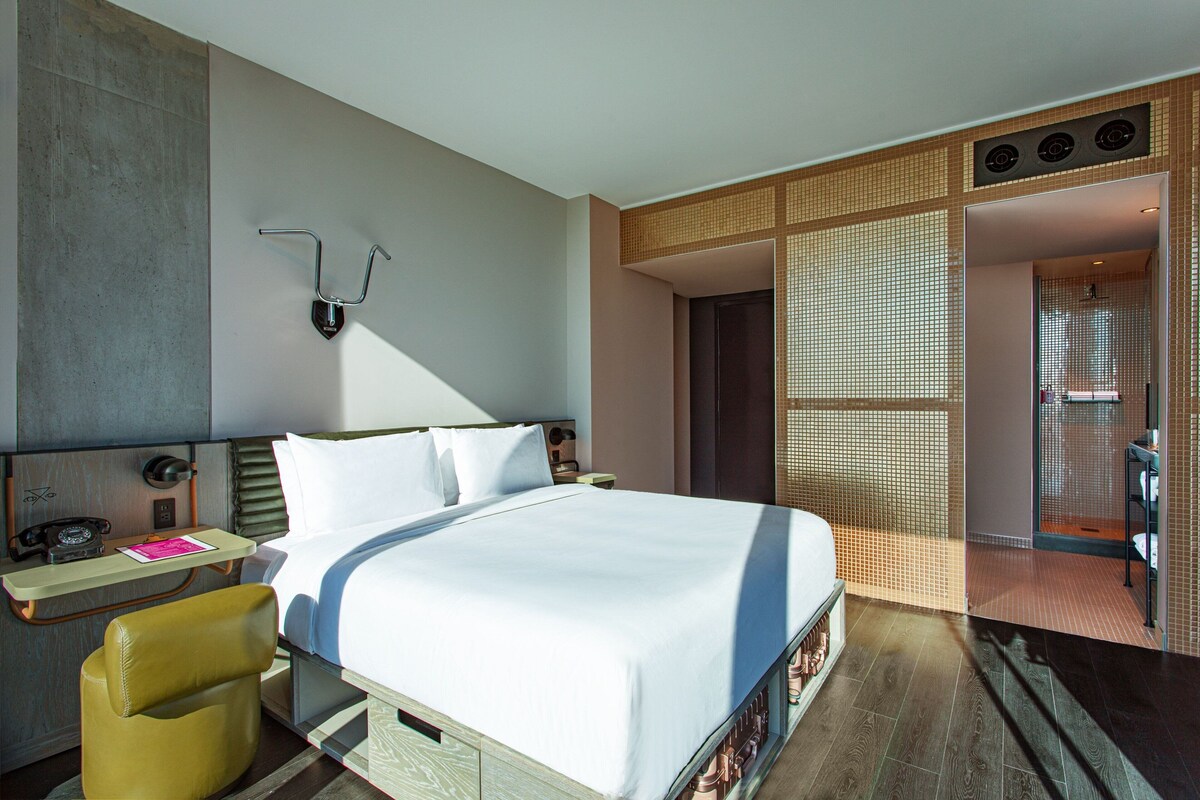Una habitación de hotel moderna con una cama grande, un escritorio con teléfono y una silla.