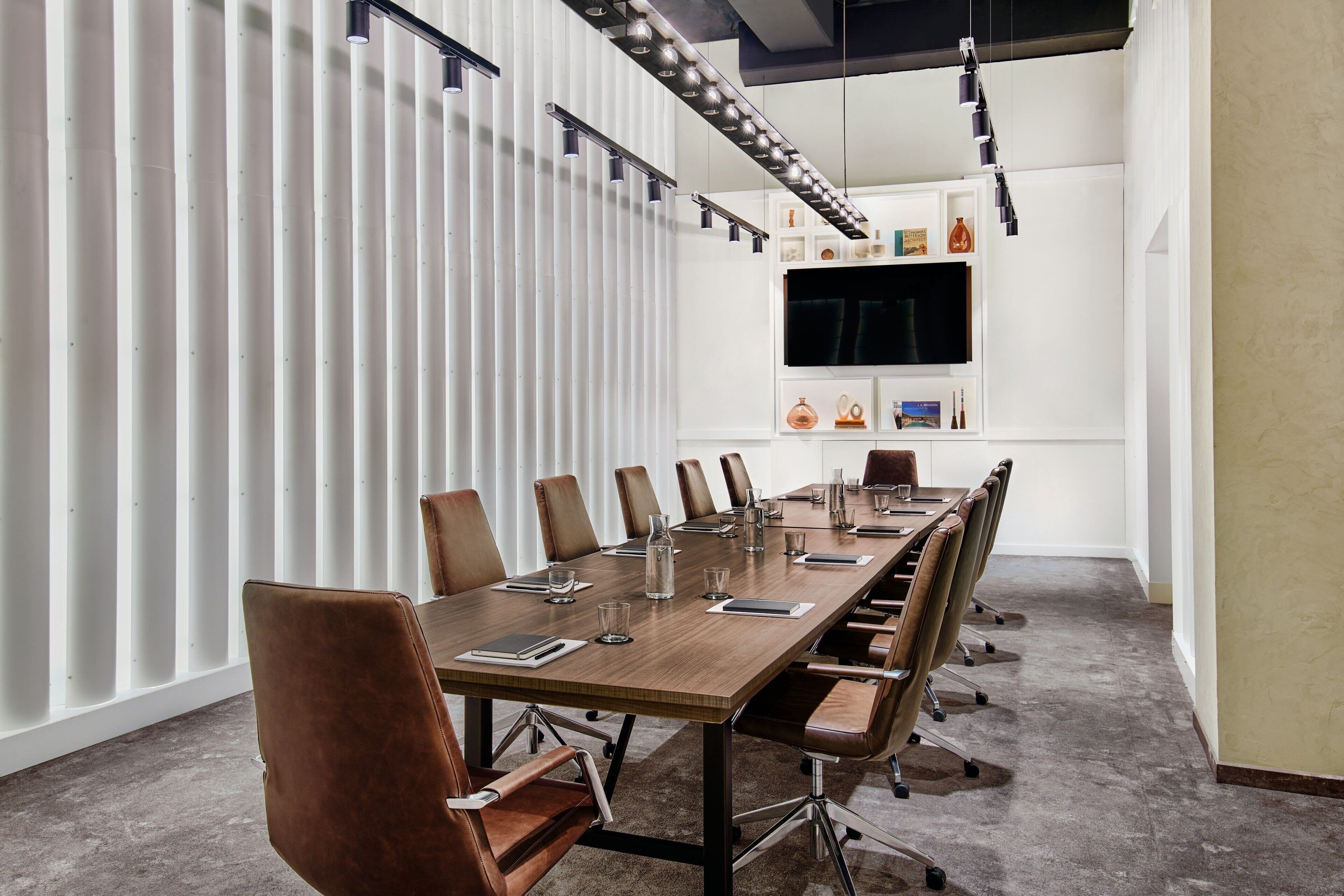 A conference room with a long table, chairs, a TV on the wall, and a white partition.