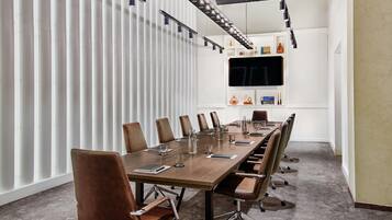 A conference room with a long table, chairs, a TV on the wall, and a white partition.