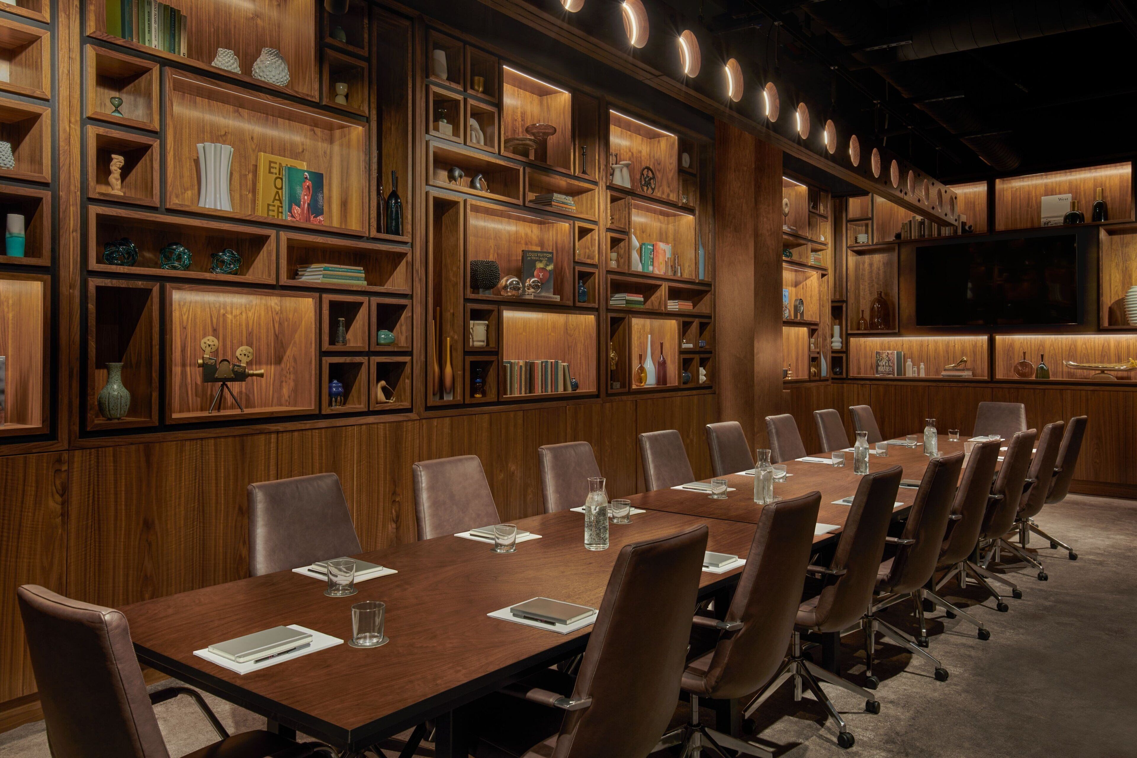 A conference room with a long table, multiple chairs, and wooden shelving with various items.