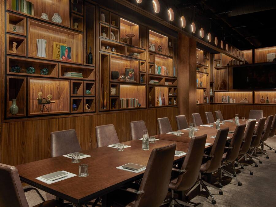 A conference room with a long table, multiple chairs, and wooden shelving with various items.