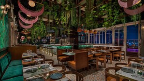 Un restaurante con asientos tapizados en verde, mesas de madera y plantas colgantes.