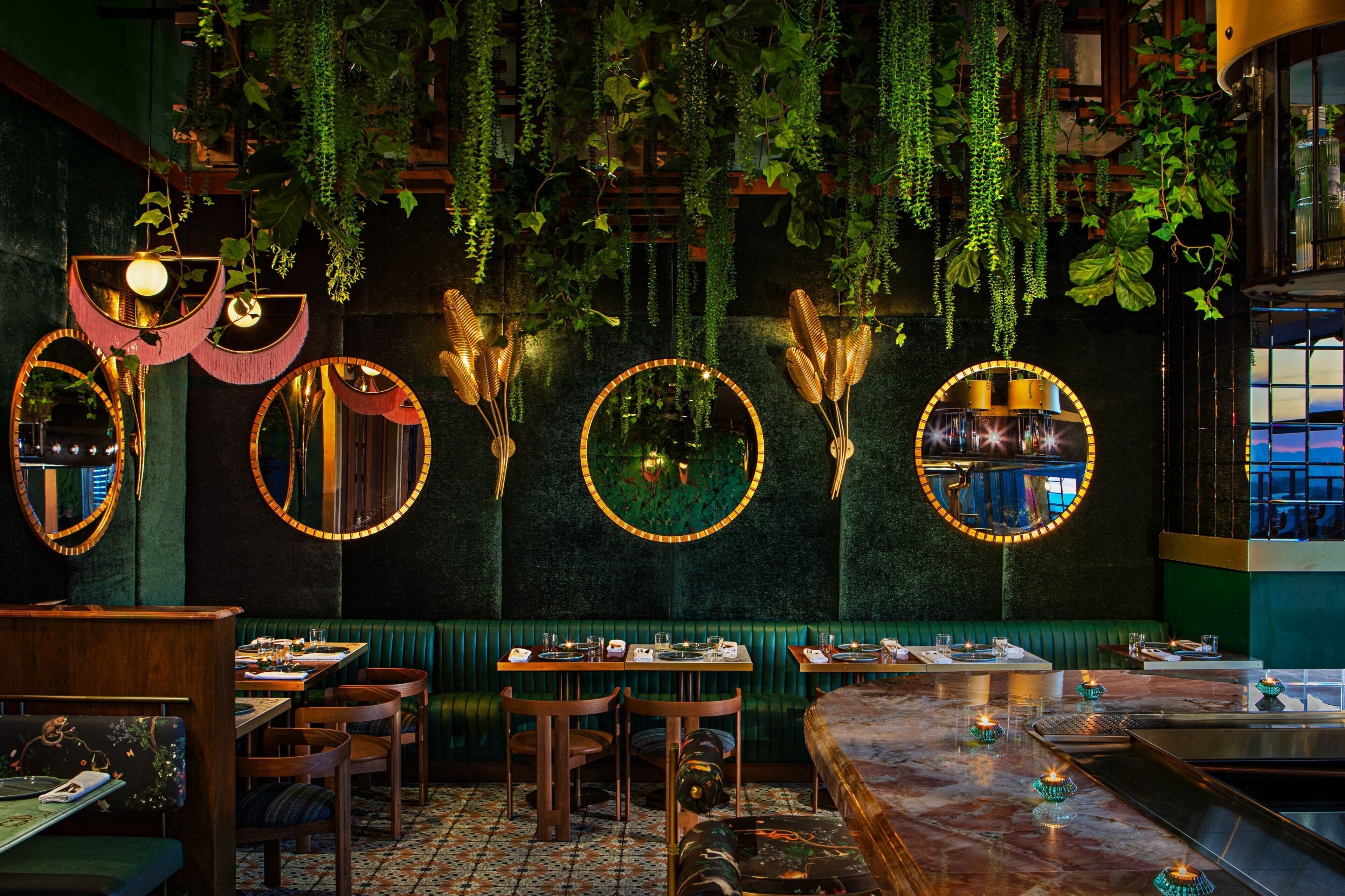 A restaurant with round mirrors, hanging plants, and a marble bar.