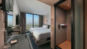 Habitación de hotel con dos camas, un escritorio con espejo, televisión y un amplio ventanal con vistas a la ciudad.