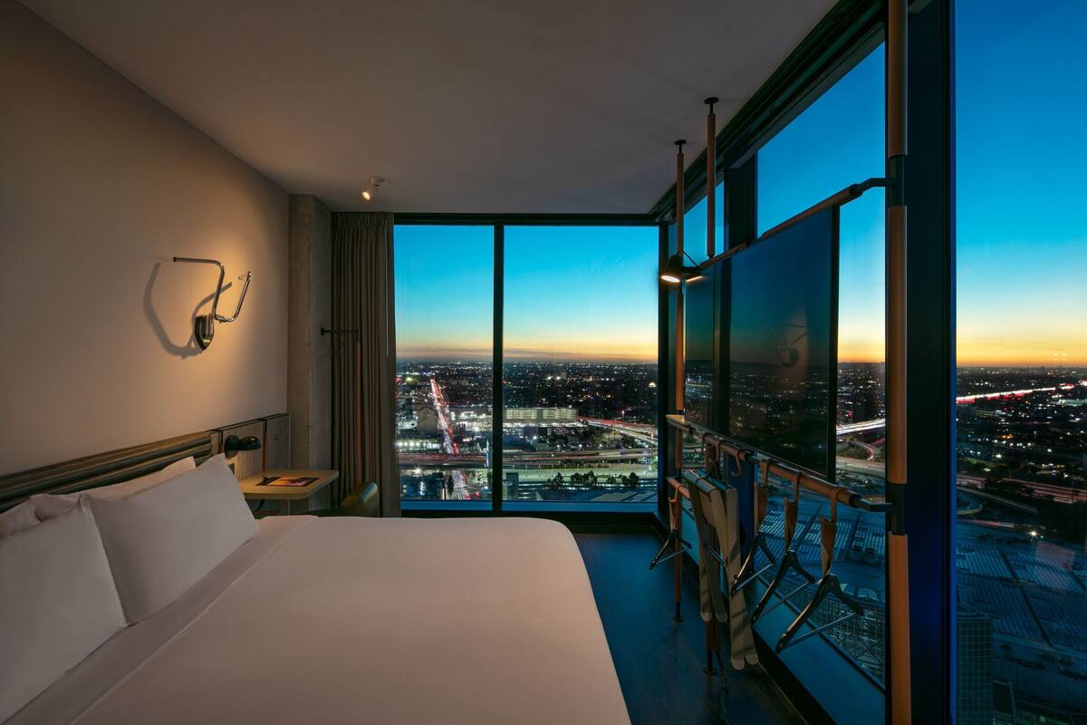Ein Hotelzimmer mit einem großen Bett, einem Schreibtisch und Blick auf die Stadt im Abenddämmerung.