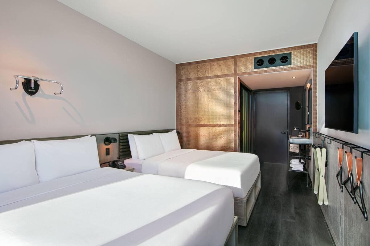 Ein Hotelzimmer mit zwei Betten, einem Badezimmer mit Spiegel und einem an der Wand befestigten Fernseher.