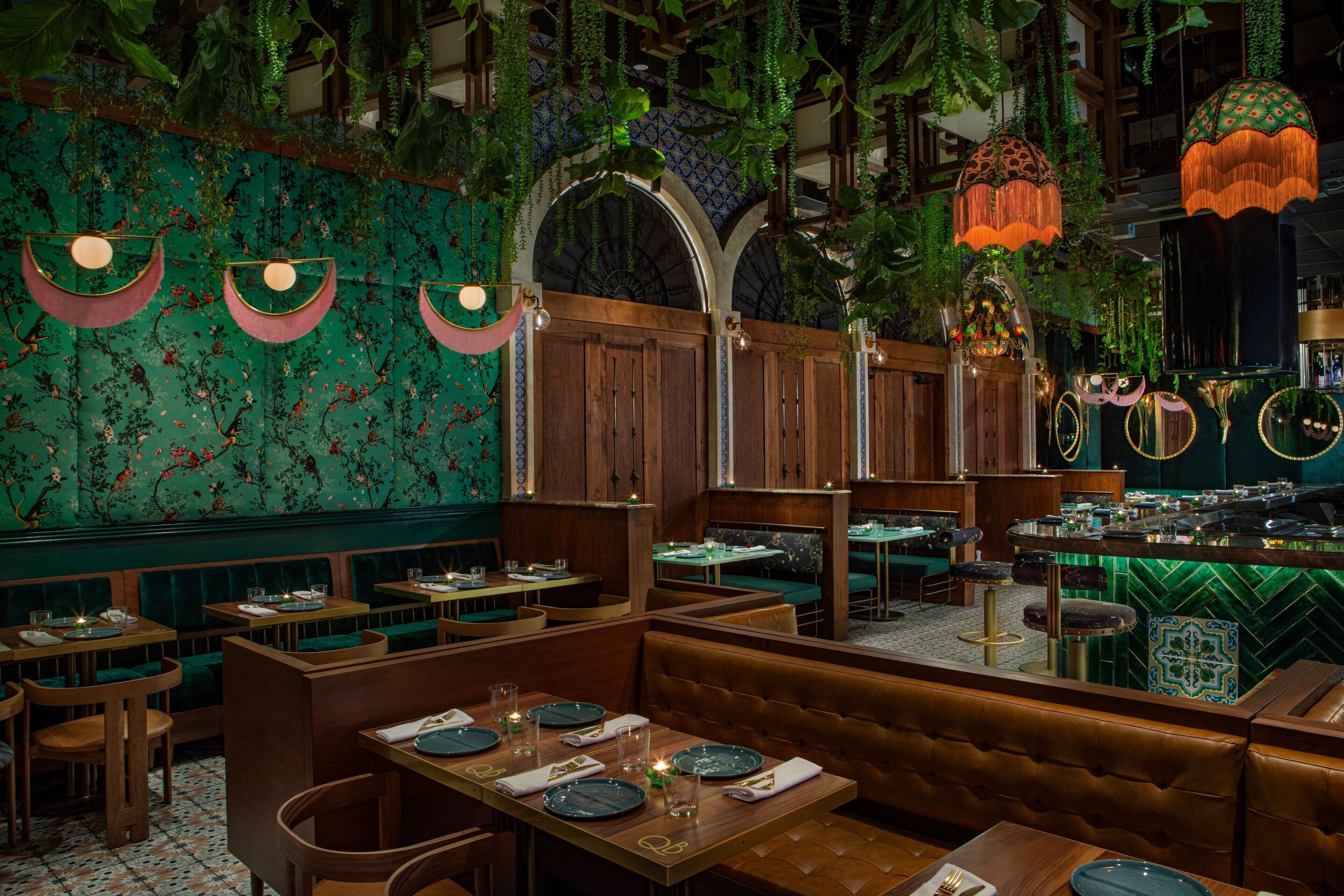 Ein Restaurant mit Sitzecken und Tischen, Holzvertäfelung, hängenden Pflanzen und einer Wand mit grünen Fliesen.