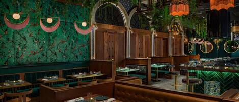 A restaurant with booths and tables, wooden paneling, hanging plants, and a green tiled wall.