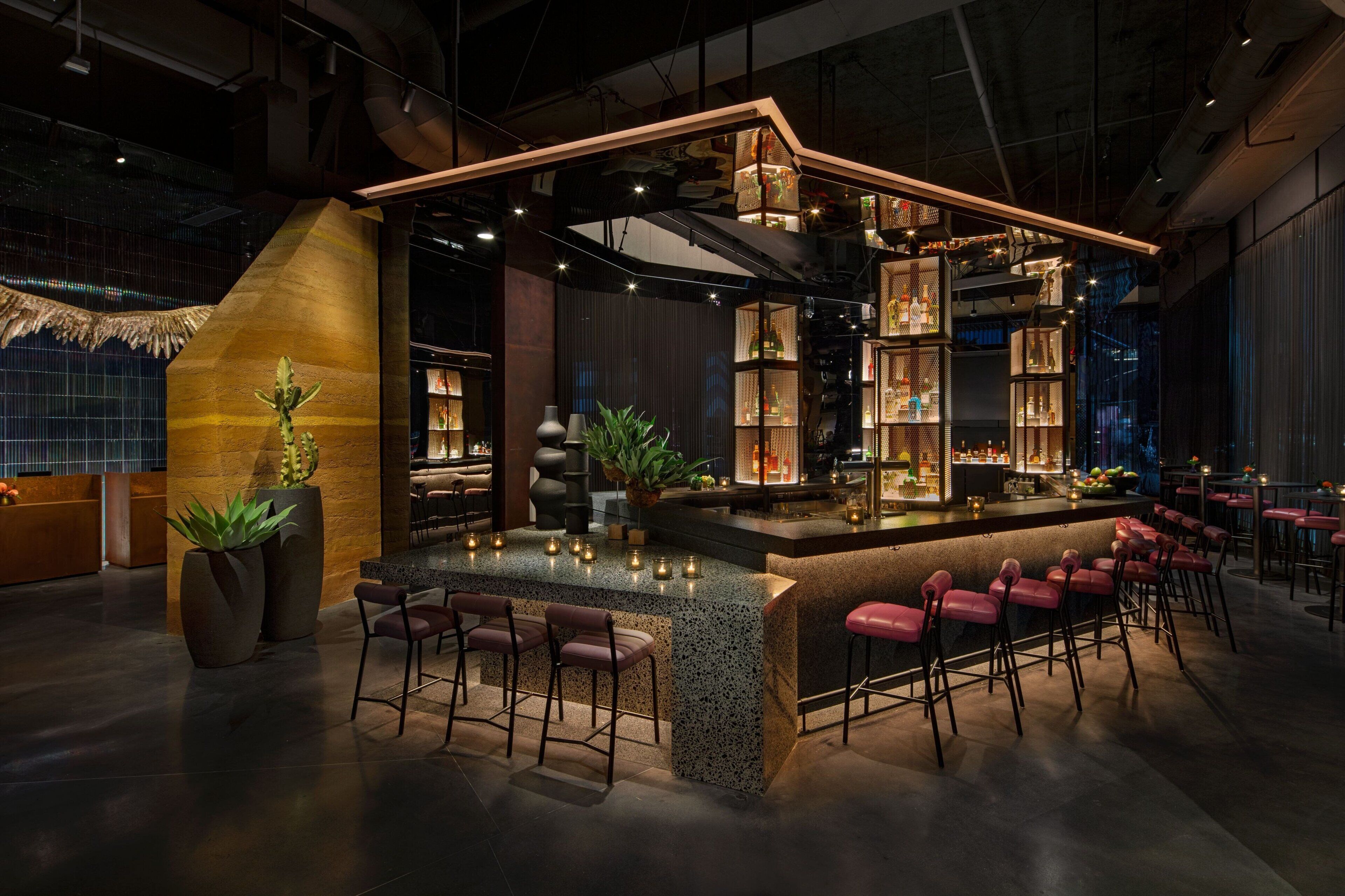 A modern bar area with a central island, bar stools, and shelves with bottles.