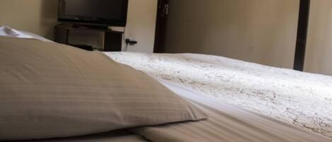 Habitación de hotel con una cama, un televisor sobre un soporte y una puerta.