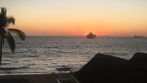 Une vue sur la plage avec un coucher de soleil, des palmiers et un bateau au loin.