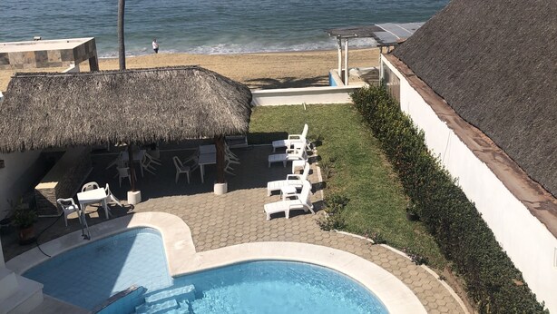 Un espace piscine avec des chaises longues, une structure Ă toit de chaume et une vue sur lâocĂ©an, oĂč lâon aperçoit un cargo.