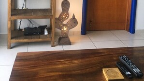 Un salon dotĂ© dâun tĂ©lĂ©viseur Ă Ă©cran plat fixĂ© au mur, dâun meuble de rangement en bois contenant des appareils Ă©lectroniques, dâune sculpture mĂ©tallique dĂ©corative, dâune porte en bois avec un cadre bleu et dâune table basse sur laquelle reposent des tĂ©lĂ©commandes.