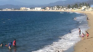 Une plage oĂč lâon voit des gens se promener le long du rivage, un ciel dĂ©gagĂ© et des montagnes Ă lâhorizon.