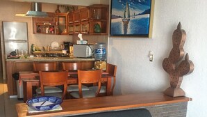 Un espace de vie compact comprenant un coin cuisine, un coin repas et un canapĂ© agrĂ©mentĂ© dâun plaid aux couleurs vives.