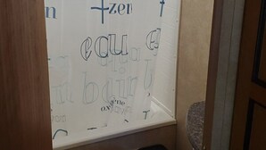 A small bathroom with a toilet, a shower curtain with text, and a black trash bin. - Trailer on Spacious lakefront Campground (Lone Butte)