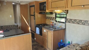 A compact RV kitchen with wooden cabinets, a stove, a microwave, and a sink. - Trailer on Spacious lakefront Campground (Lone Butte)