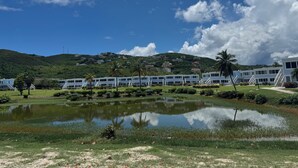Un hotel con piscina, rodeado de vegetación y una colina al fondo.