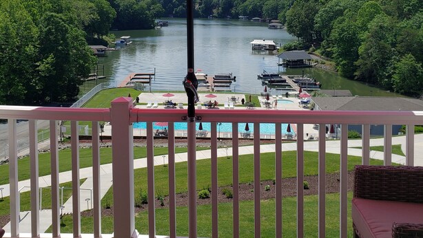 Un balcón con sombrilla roja, con vistas a un lago con barcos, piscina y abundante vegetación.