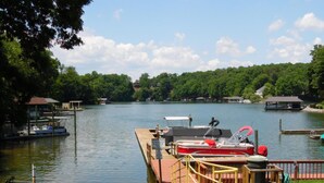 Un muelle con barcos, un paseo marítimo de madera y una vista de un lago rodeado de árboles y casas.