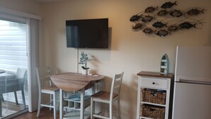 Una cocina compacta con una mesa y sillas de madera, un armario blanco con cestas, un televisor de pantalla plana y un refrigerador.