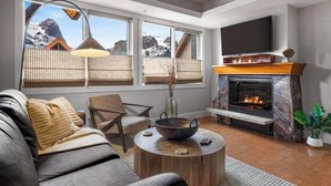 A modern living room with a fireplace, comfortable seating, and large windows offering mountain views. - Rundle Rock Retreat | Majestic Views - Luxury Condo (Canmore)