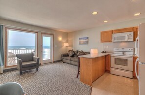 Une chambre avec vue sur l’océan, une kitchenette équipée d’un four à micro-ondes et d’un four traditionnel, un canapé avec des coussins et un fauteuil.