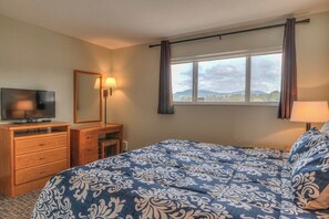 A bedroom with a bed, a television, a desk, and a window with curtains. - Oceanfront One Bedroom Suite, Stunning Views & King Bed! (Lincoln City)