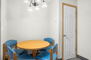A room with a round wooden table, four blue chairs, a white door, and a ceiling light fixture.