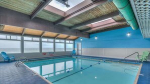 Piscina interior con ventanas transparentes, sillas azules y verdes, y una pared azul y blanca.