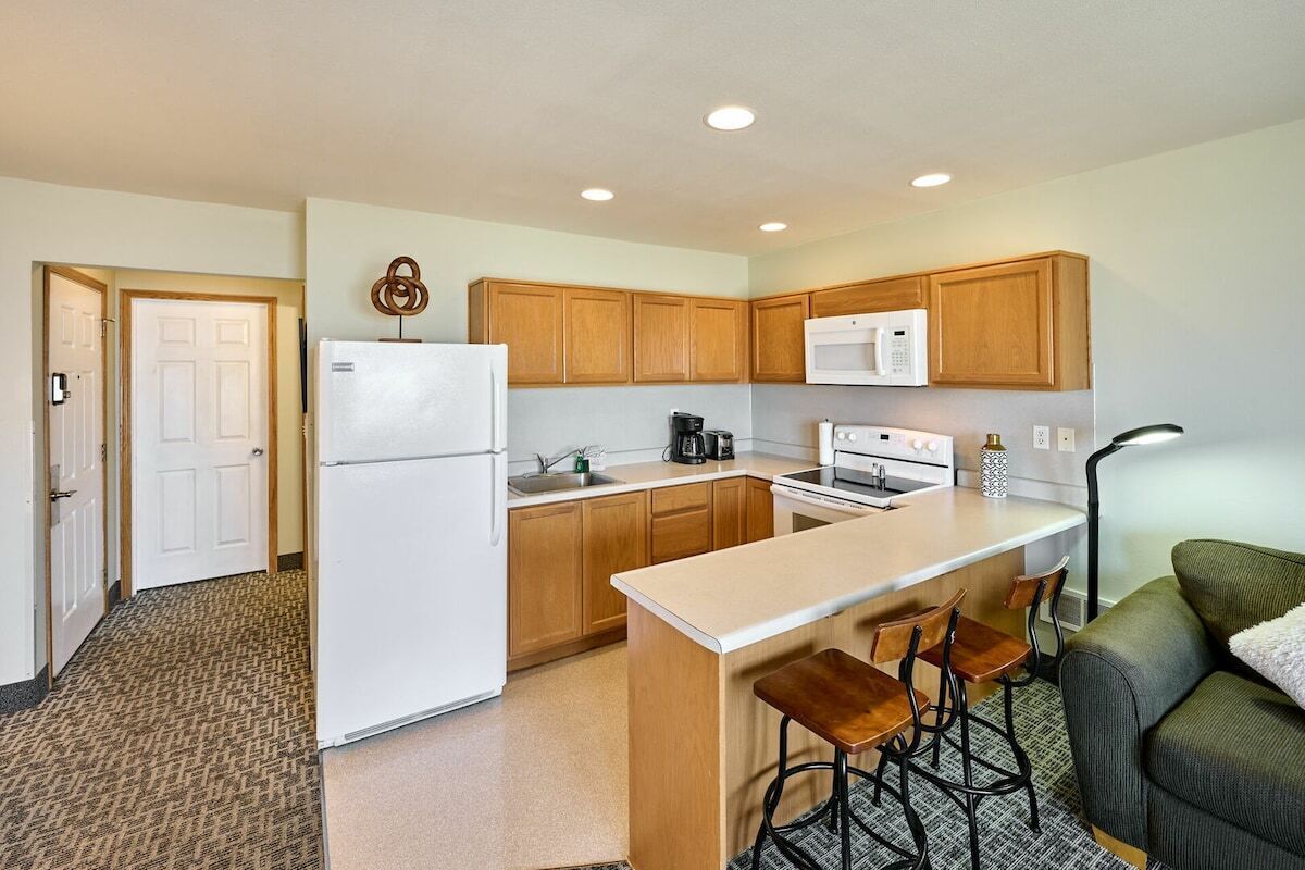 A compact kitchen with wooden cabinets, a white refrigerator, a microwave, and a coffee maker.