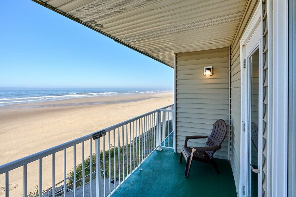 Un balcon avec vue sur la plage, une chaise et une petite table.