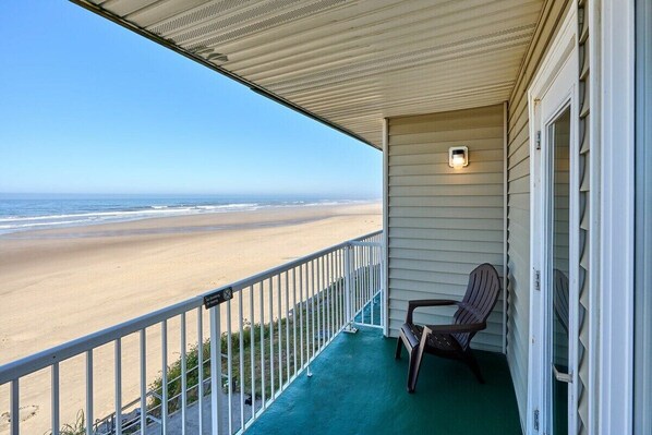 Un balcón con vista a la playa, una silla y una mesita.